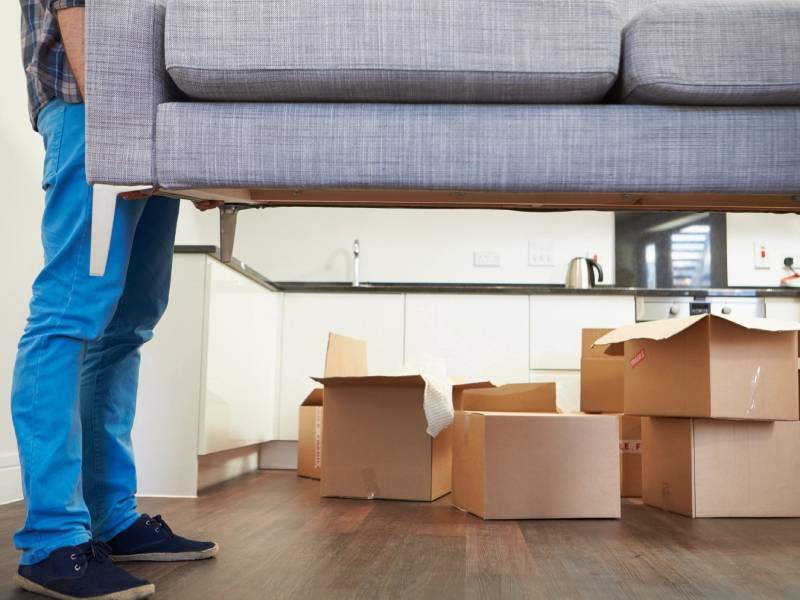 Man holding up a sofa with moving boxes in the background