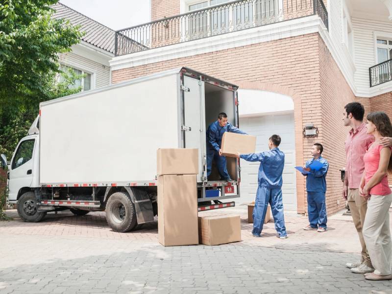 Three men moving boxes out of a work van while a happy couple watches